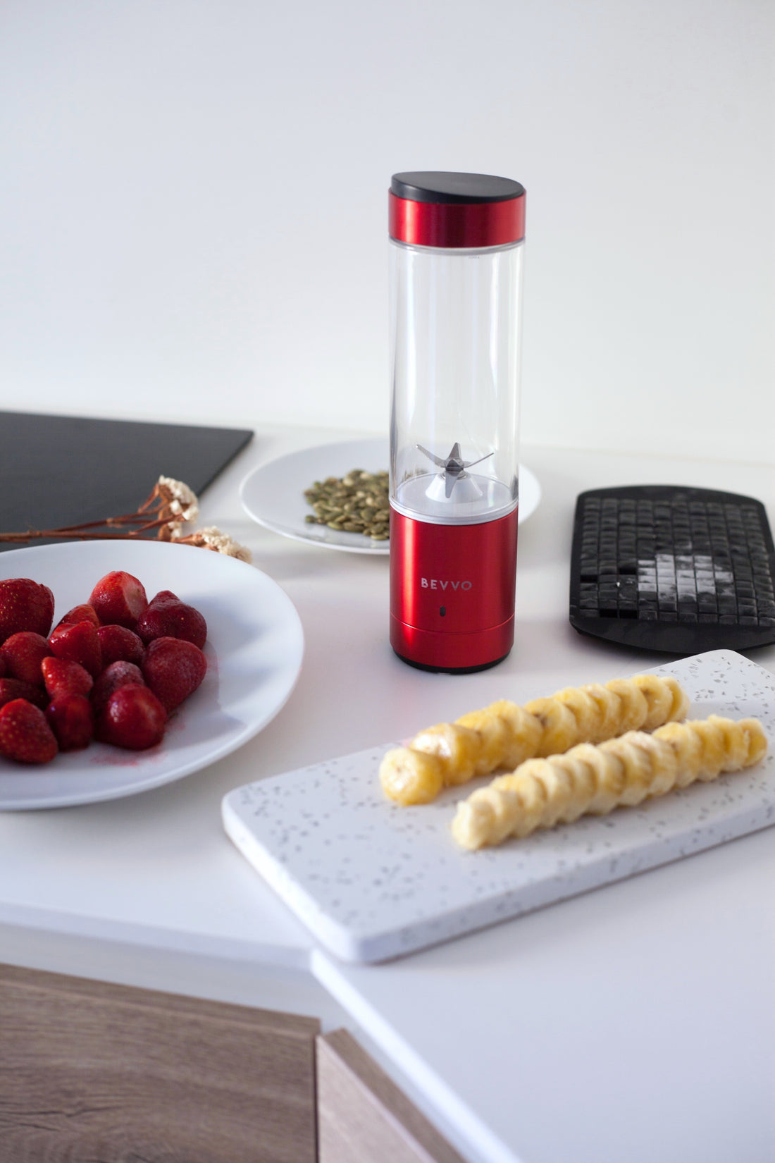 Red BEVVO Blender on kitchen counter with smoothie ingredients being prepped
