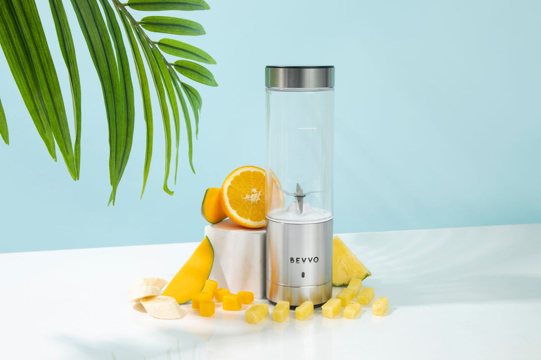 Silver BEVVO portable blender surrounded by tropical fruit including mango, pineapple, orange and banana.